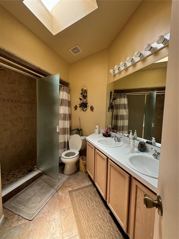 A bathroom features a double vanity, a walk-in shower, a toilet, and a skylight — 105 CATTAIL COURT, KISSIMMEE, FL
