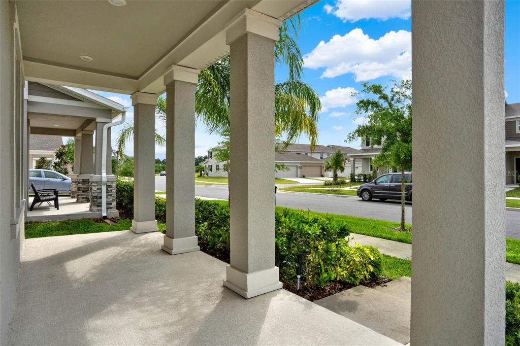 A covered front porch with concrete flooring and square columns overlooks a suburban street — 8114 SAYINGS DRIVE, WINTER GARDEN, FL
