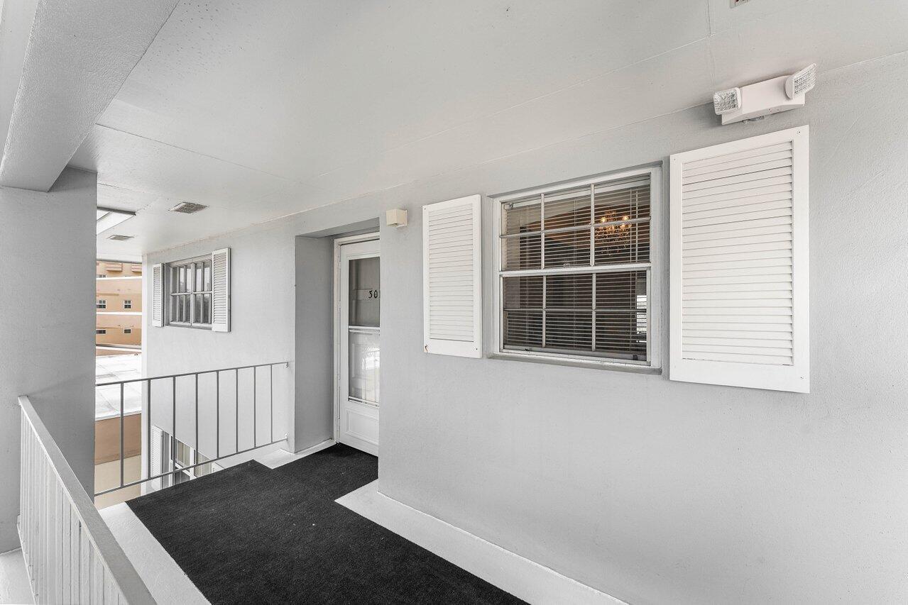 An exterior walkway leads to a white door and window with shutters on a building — 157 Atlantis Boulevard # 301, Atlantis FL 33462, ATLANTIS, FL