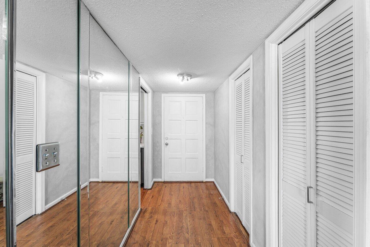 A hallway with wood-look flooring, mirrored closet doors, and a white front door — 157 Atlantis Boulevard # 301, Atlantis FL 33462, ATLANTIS, FL