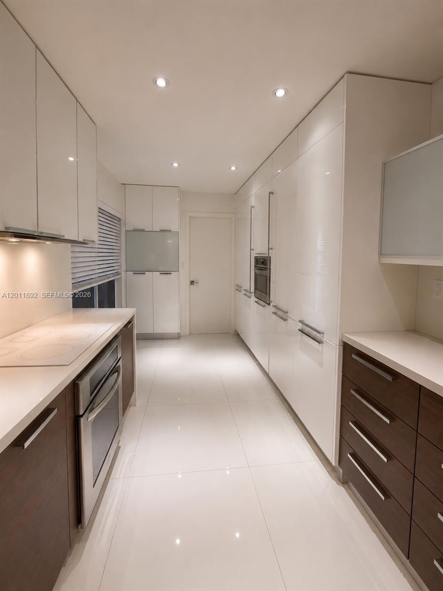 A modern galley kitchen features white glossy cabinets, dark wood lower drawers, and white countertops — 9871 NW 52nd Ln # 0, Doral FL 33178, DORAL, FL