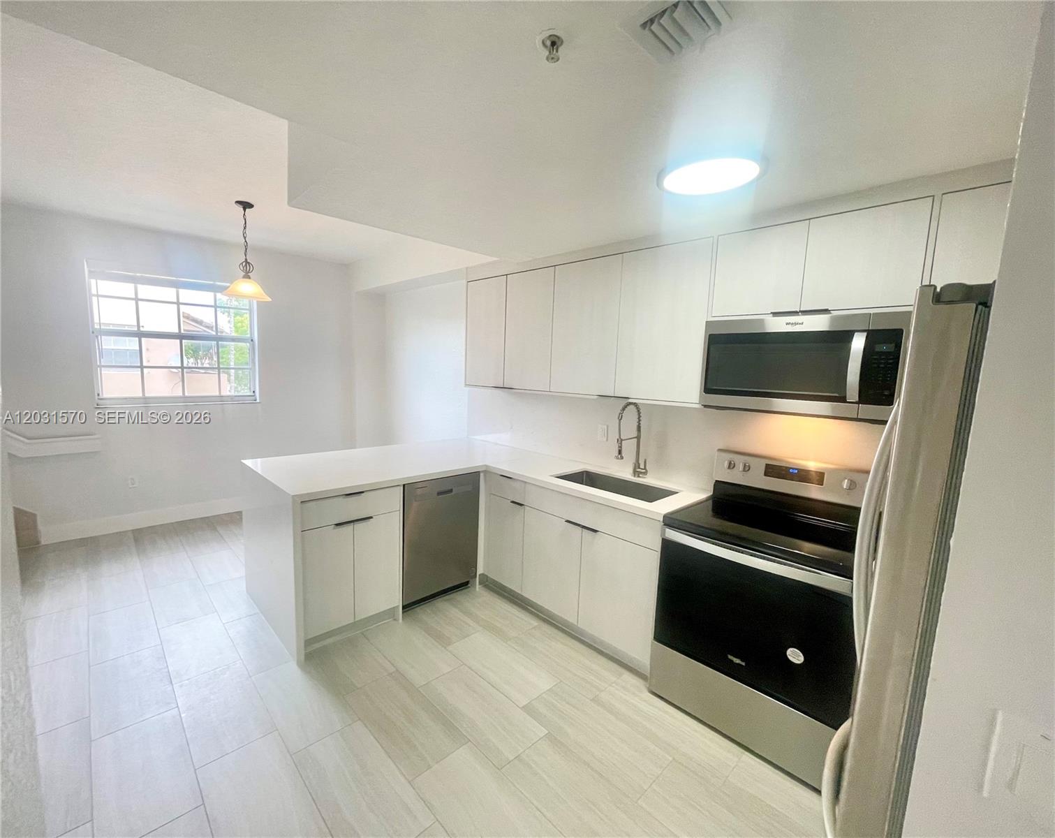 A modern kitchen features white cabinetry, quartz countertops, stainless steel appliances, and light-colored flooring — 77 E 4th St # A212, Hialeah FL 33010, HIALEAH, FL