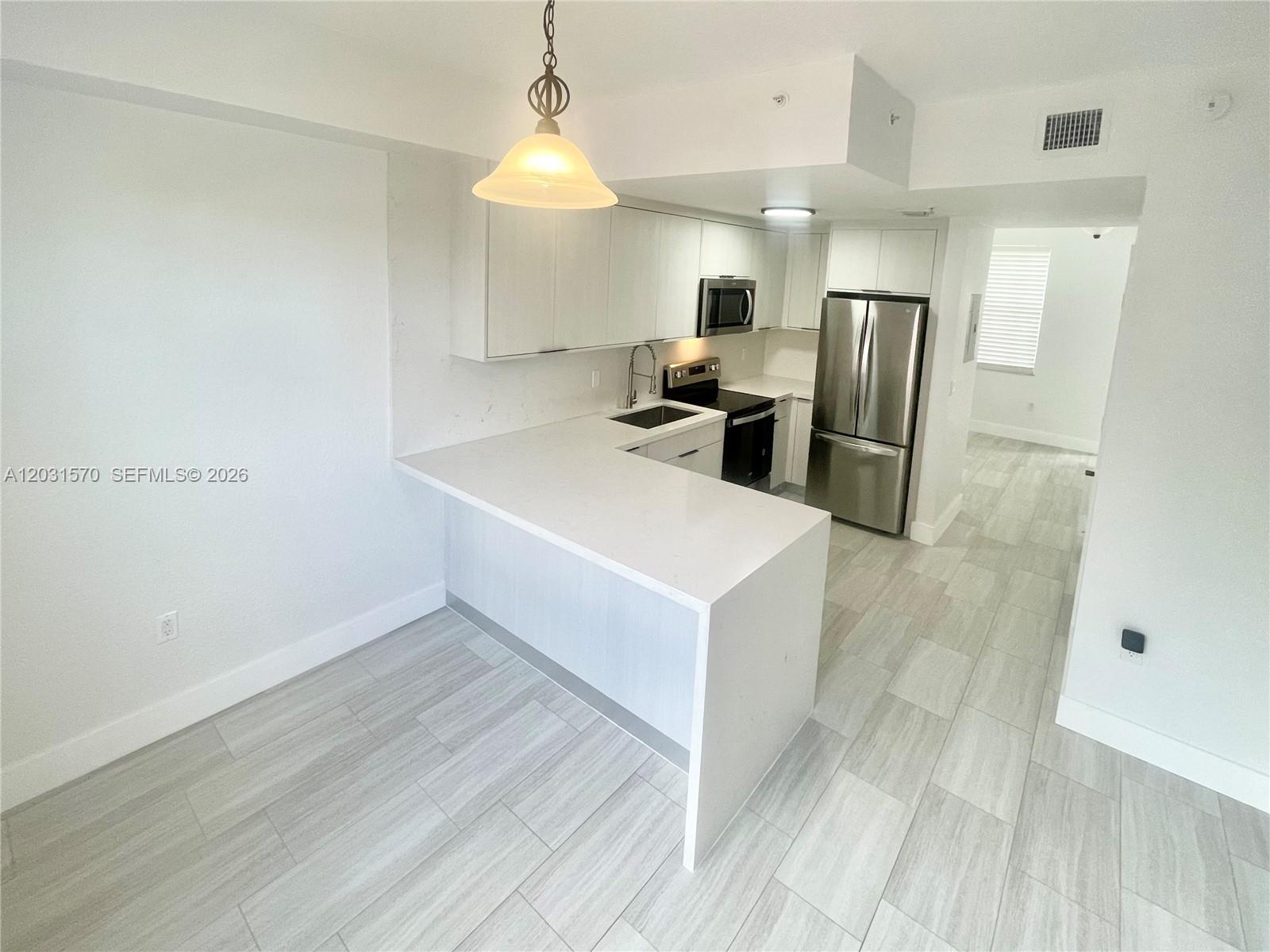 A modern kitchen features white cabinets, stainless steel appliances, and a white quartz countertop — 77 E 4th St # A212, Hialeah FL 33010, HIALEAH, FL