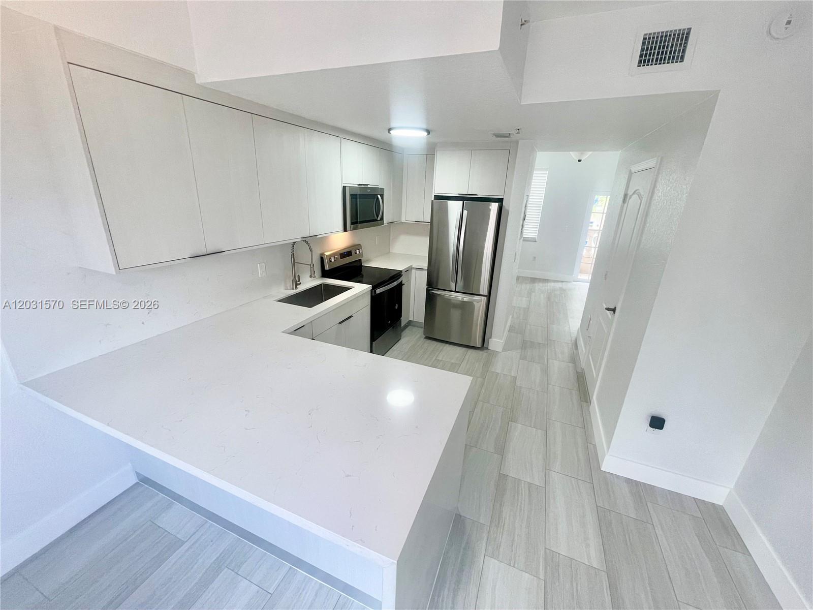 A kitchen with white cabinets and a peninsula sits next to a tiled staircase — 77 E 4th St # A212, Hialeah FL 33010, HIALEAH, FL