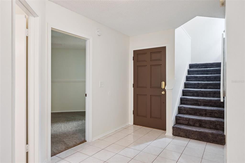 An entryway with white tile flooring, a brown front door, and carpeted stairs leading upward — 467 CIDERMILL PLACE, LAKE MARY, FL