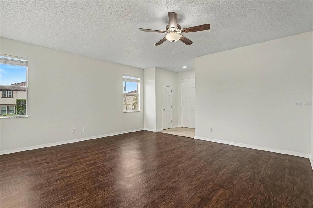 An empty room features dark wood-look flooring, white walls, a ceiling fan, and two windows — 4542 GALLBERRY COURT, ORLANDO, FL