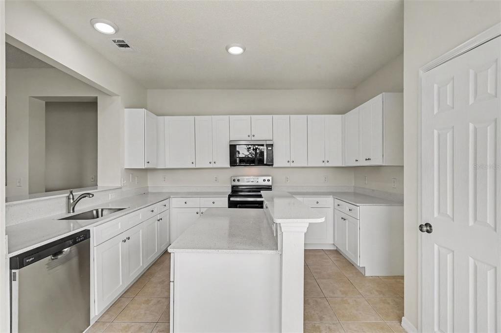 A white kitchen features a central island, stainless steel appliances, and light-colored tile flooring — 4542 GALLBERRY COURT, ORLANDO, FL