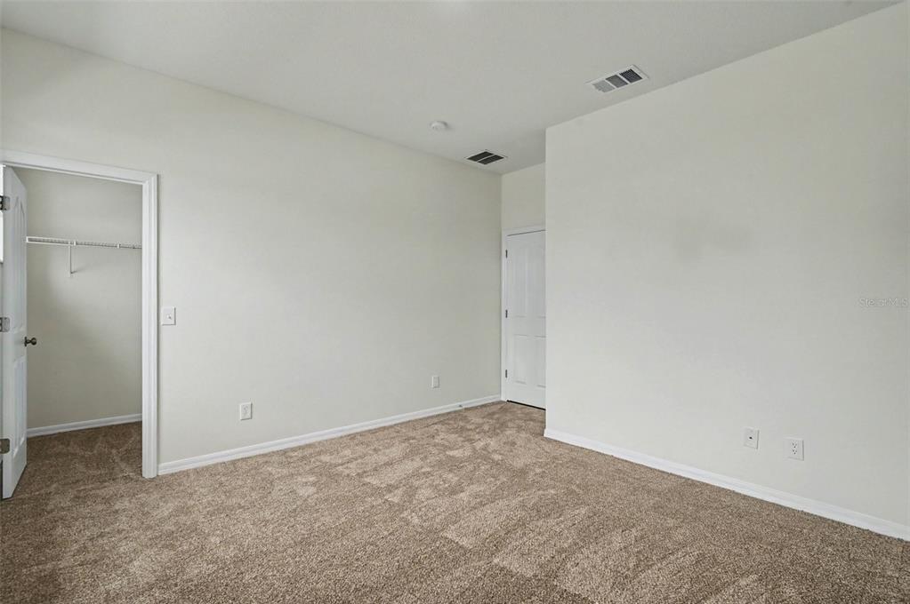 An empty bedroom features beige carpeting, white walls, a walk-in closet, and a closed door — 4542 GALLBERRY COURT, ORLANDO, FL