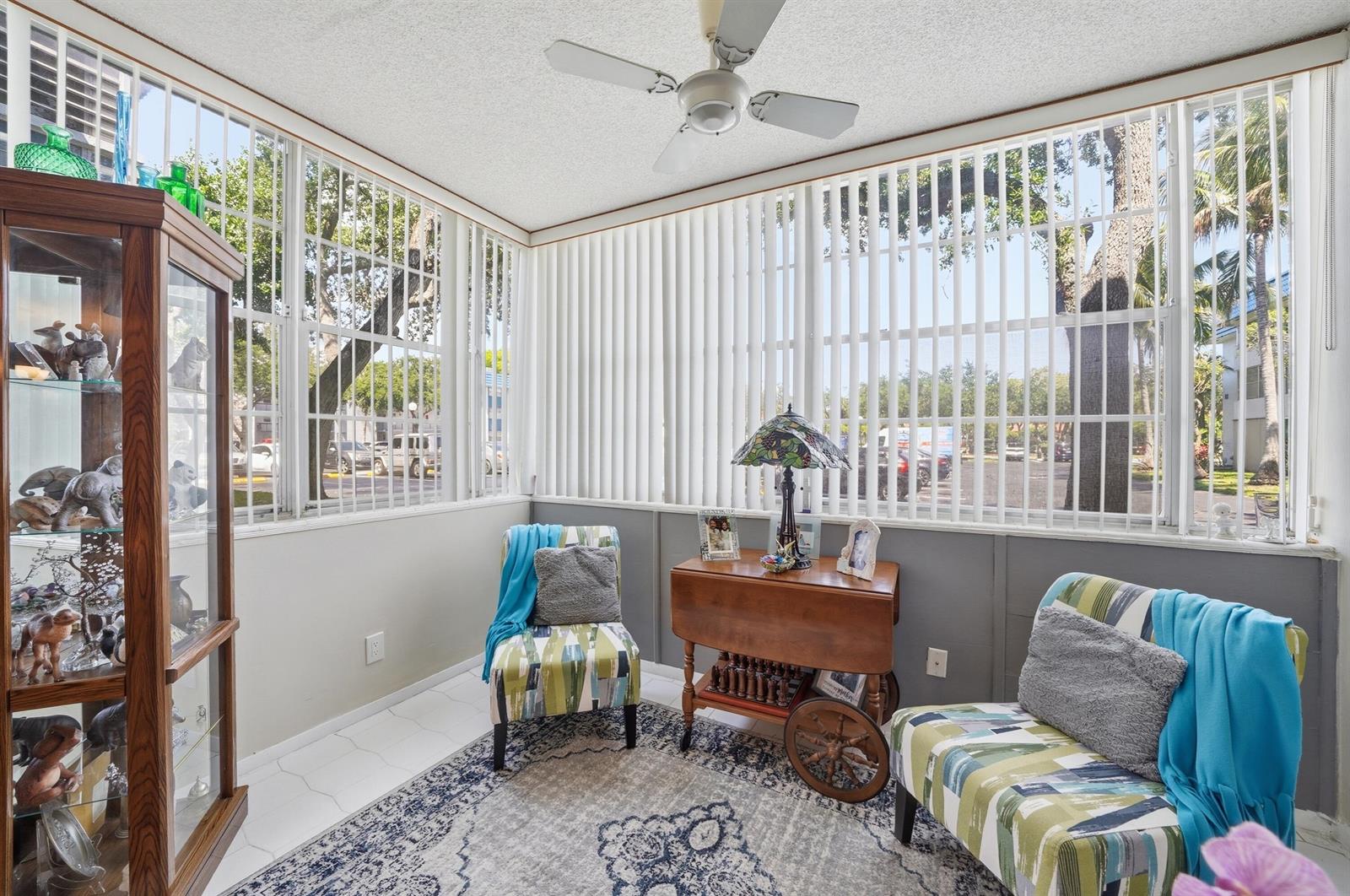 A sunroom features a patterned rug, two armchairs, a wooden side table, and large windows — 3130 Holiday Springs Boulevard # 103, Margate FL 33063, MARGATE, FL