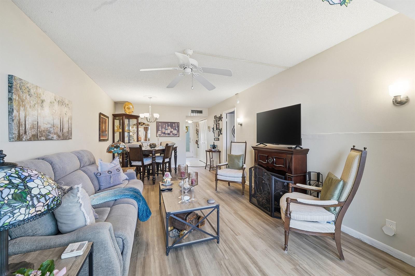 A living room features light wood-look flooring, a grey sofa, a TV console, and dining area — 3130 Holiday Springs Boulevard # 103, Margate FL 33063, MARGATE, FL