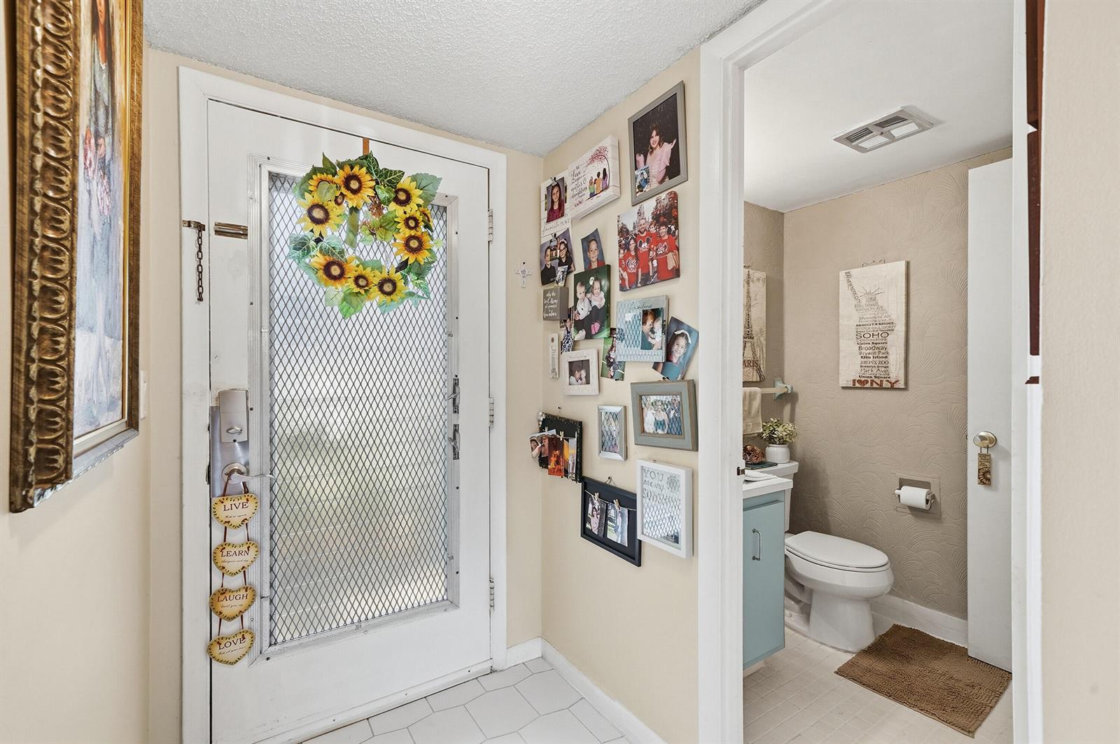A home entryway features a white door with a sunflower wreath and a nearby bathroom — 3130 Holiday Springs Boulevard # 103, Margate FL 33063, MARGATE, FL