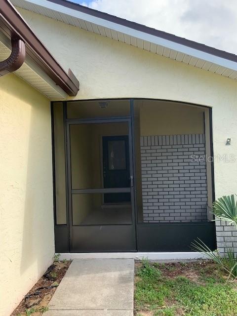 A screened-in entryway features a dark metal door and a gray brick accent wall — 7817 LAUREL OAK LANE, KISSIMMEE, FL