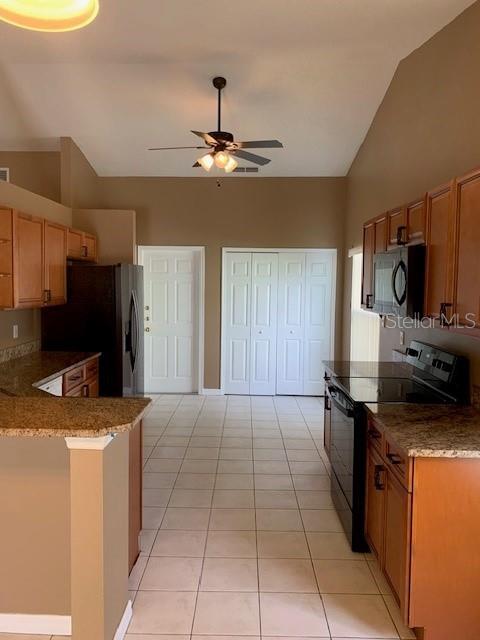 A kitchen features light wood cabinets, granite countertops, tile flooring, and a ceiling fan — 7817 LAUREL OAK LANE, KISSIMMEE, FL