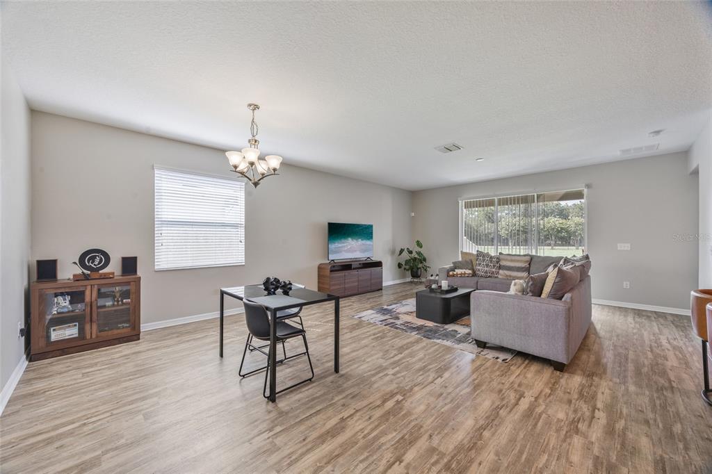An open-concept living and dining area features wood-look flooring, a gray sectional, and a television — 13801 NEWPORT SHORES DRIVE, HUDSON, FL