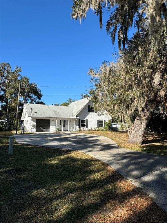 A white two-story house with a garage and a concrete driveway sits under large trees — 20164 SE 115TH COURT, INGLIS, FL