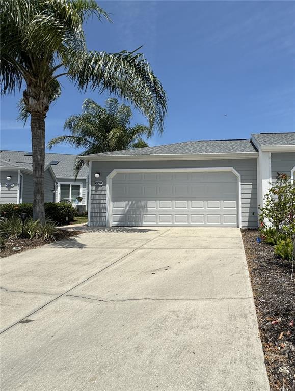 A gray-sided house features a white two-car garage door and a concrete driveway — 1005 PELICAN COURT, BRADENTON, FL