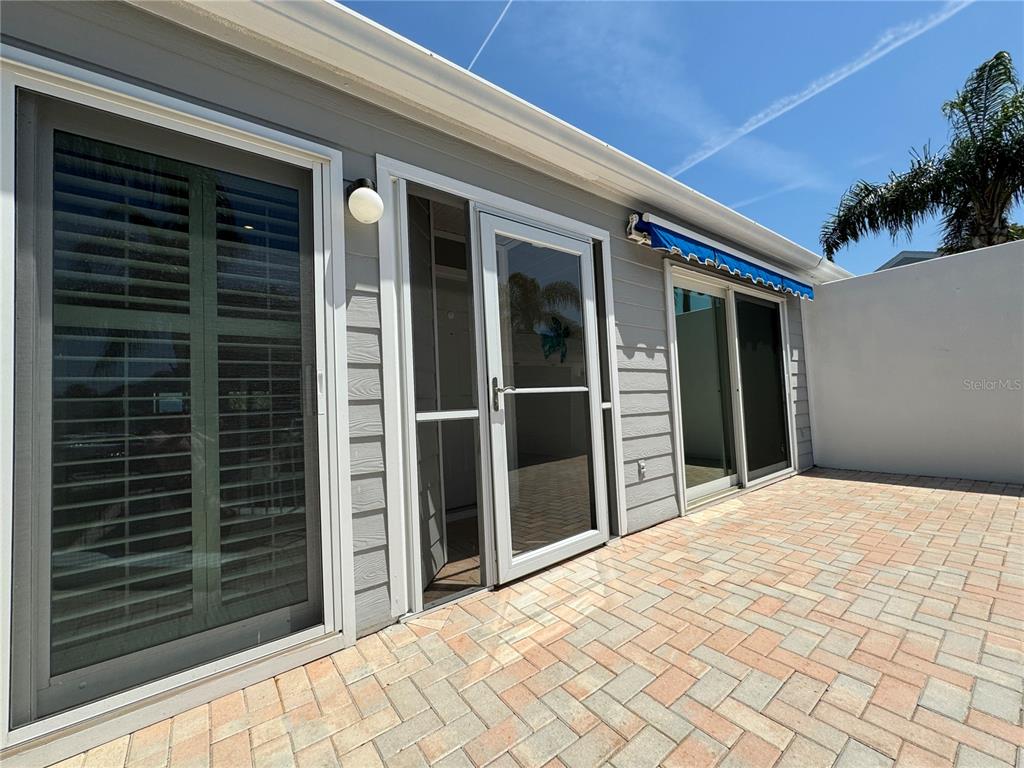 A gray-sided house exterior features a patio, a screen door, and two sliding glass doors — 1005 PELICAN COURT, BRADENTON, FL