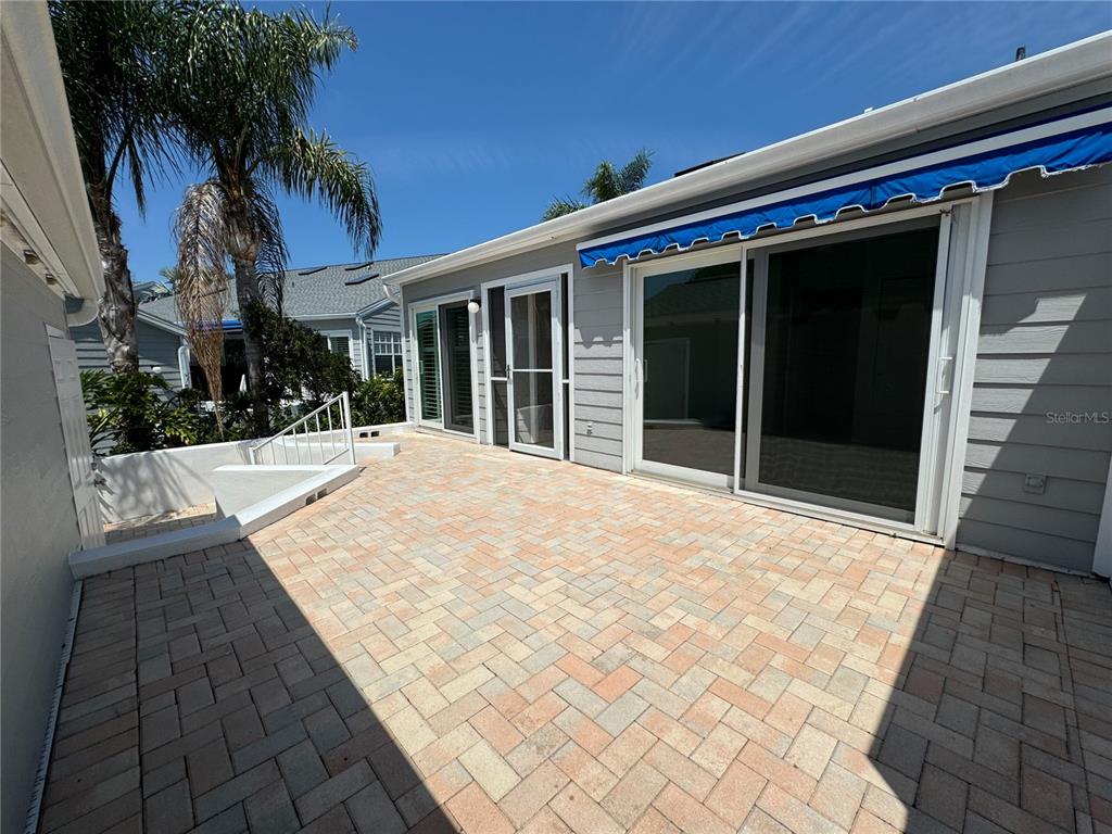 A paved patio area features a sliding glass door and a retractable blue fabric awning — 1005 PELICAN COURT, BRADENTON, FL