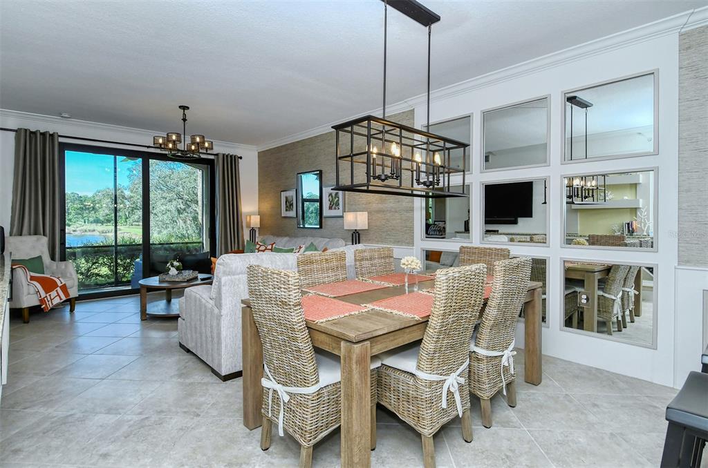 A dining area with a wicker-chair table sits adjacent to a living room with mirrors — 16706 VARDON TERRACE UNIT 105, BRADENTON, FL
