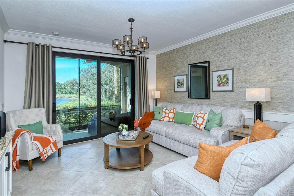 A living room features a textured accent wall, a sofa, an armchair, and sliding glass doors — 16706 VARDON TERRACE UNIT 105, BRADENTON, FL