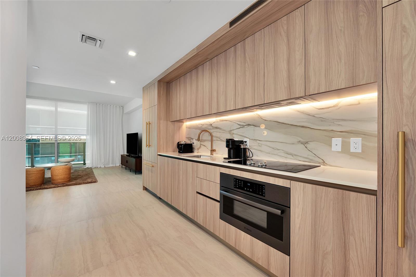 A modern kitchen features light wood cabinetry, a marble backsplash, and integrated appliances — 77 SE 5 # 1906, Miami FL 33131-2507, MIAMI, FL