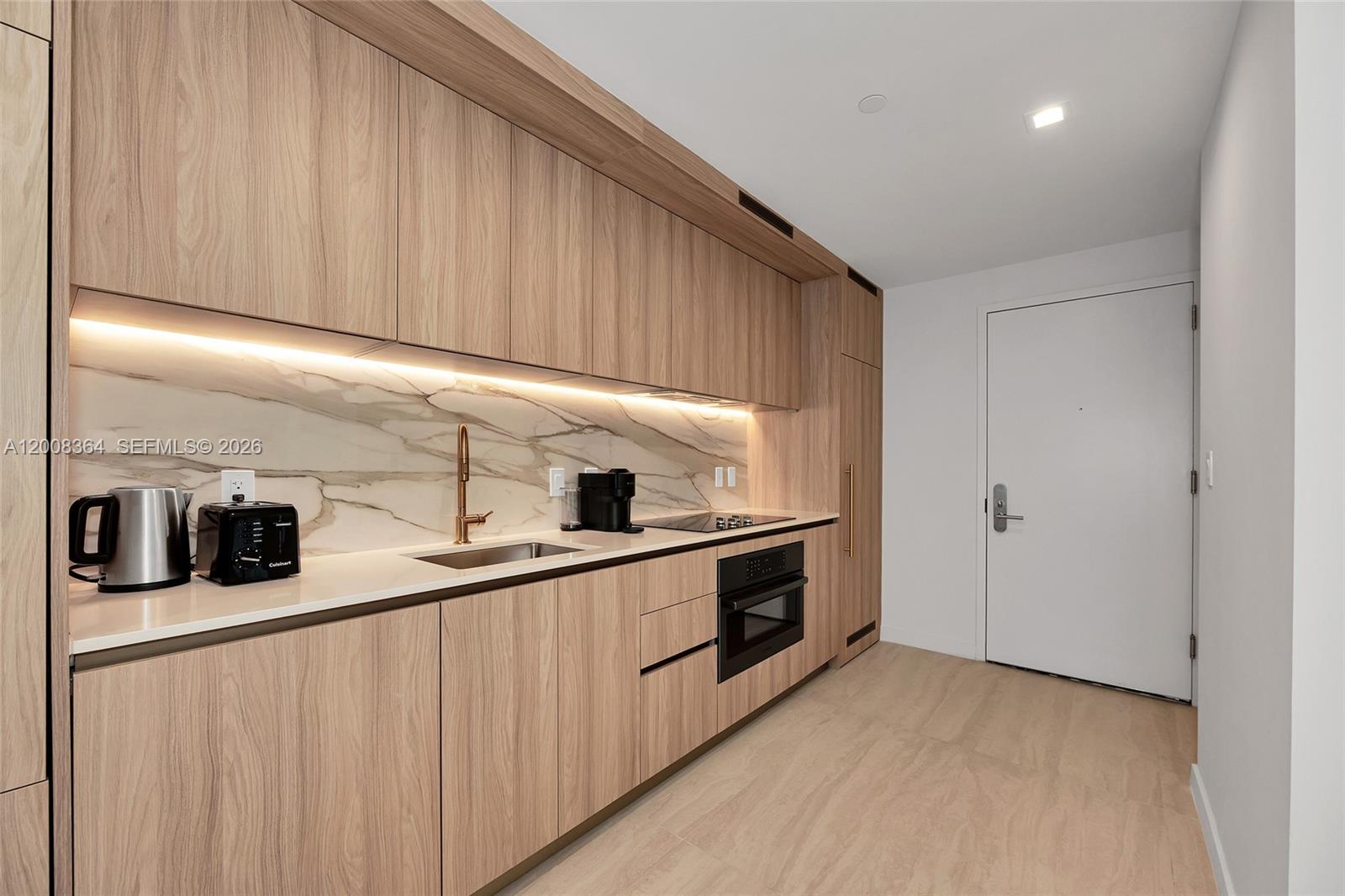 A modern kitchen features light wood cabinetry, white countertops, and a marble backsplash — 77 SE 5 # 1906, Miami FL 33131-2507, MIAMI, FL