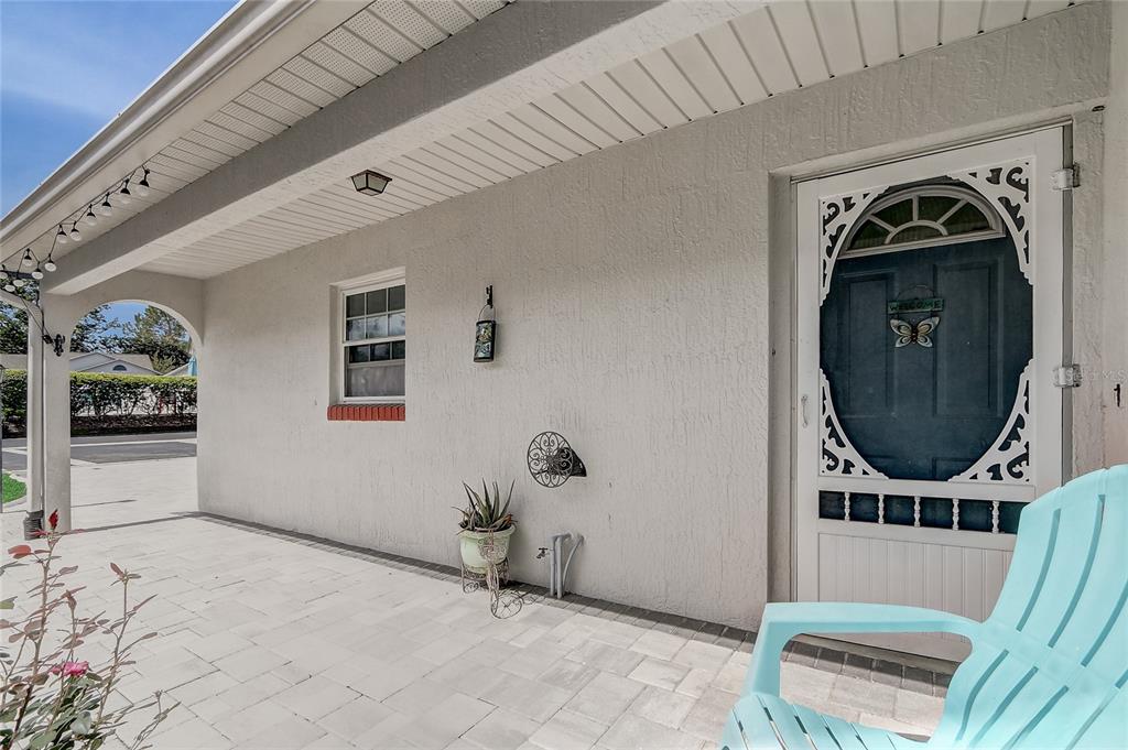 A covered patio features light-colored pavers, a blue front door with a screen, and a chair — 399 DIVISION STREET, CLERMONT, FL