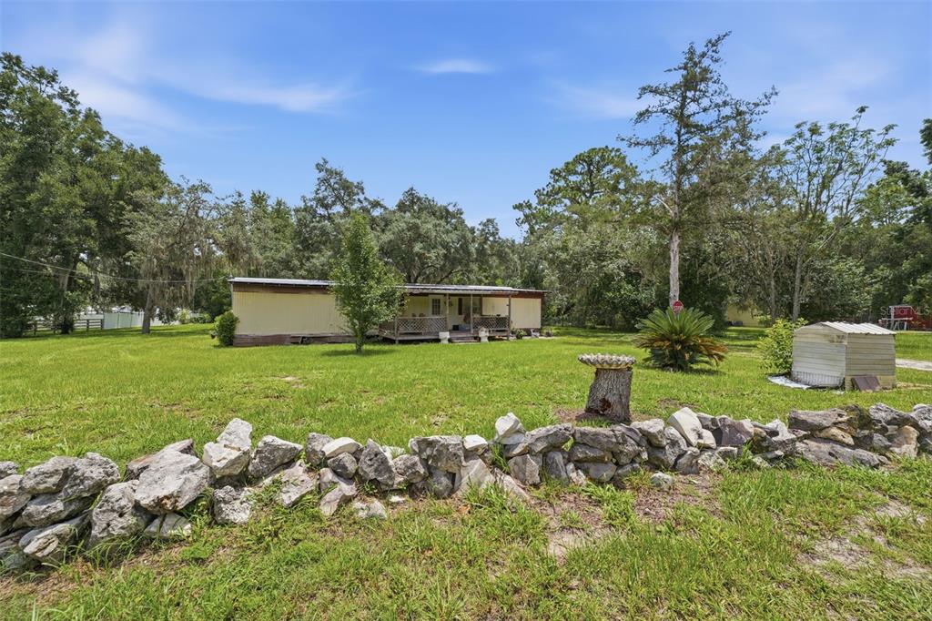 A single-story mobile home sits on a grassy lot behind a low stone wall — 6106 DESALES STREET, BROOKSVILLE, FL