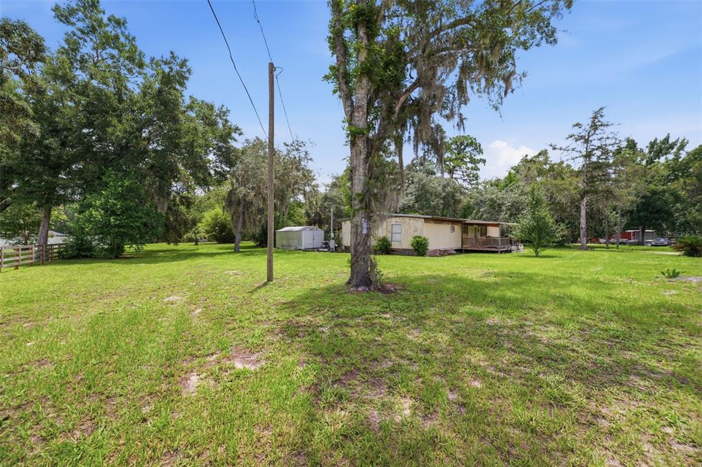 A mobile home sits on a large grassy lot with mature trees and a shed — 6106 DESALES STREET, BROOKSVILLE, FL