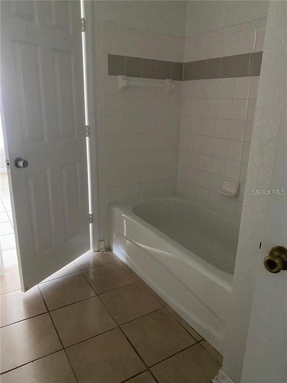 A bathroom features a white bathtub with tiled walls and a light-colored tiled floor — 3725 CASTLE PINES LANE UNIT 4337, ORLANDO, FL
