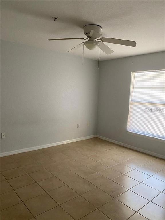 An empty room features light-colored walls, tiled flooring, a ceiling fan, and a window — 3725 CASTLE PINES LANE UNIT 4337, ORLANDO, FL