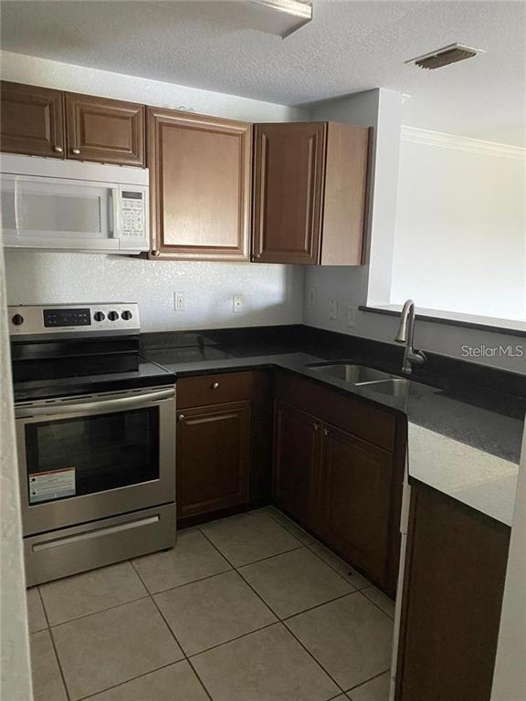 A kitchen features brown cabinets, stainless steel appliances, and dark countertops over tiled flooring — 3725 CASTLE PINES LANE UNIT 4337, ORLANDO, FL