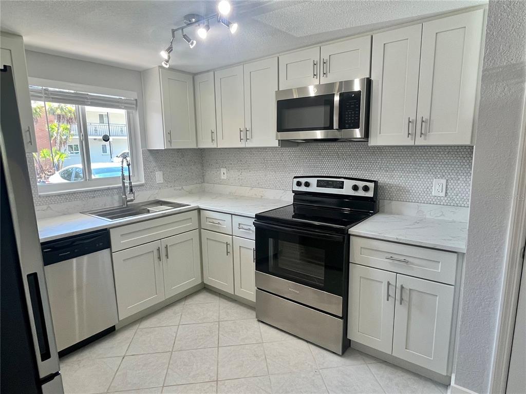 A kitchen features white cabinets, stainless steel appliances, a marble-look countertop, and a tiled backsplash — 4550 OVERLOOK DRIVE NE UNIT 156, ST PETERSBURG, FL