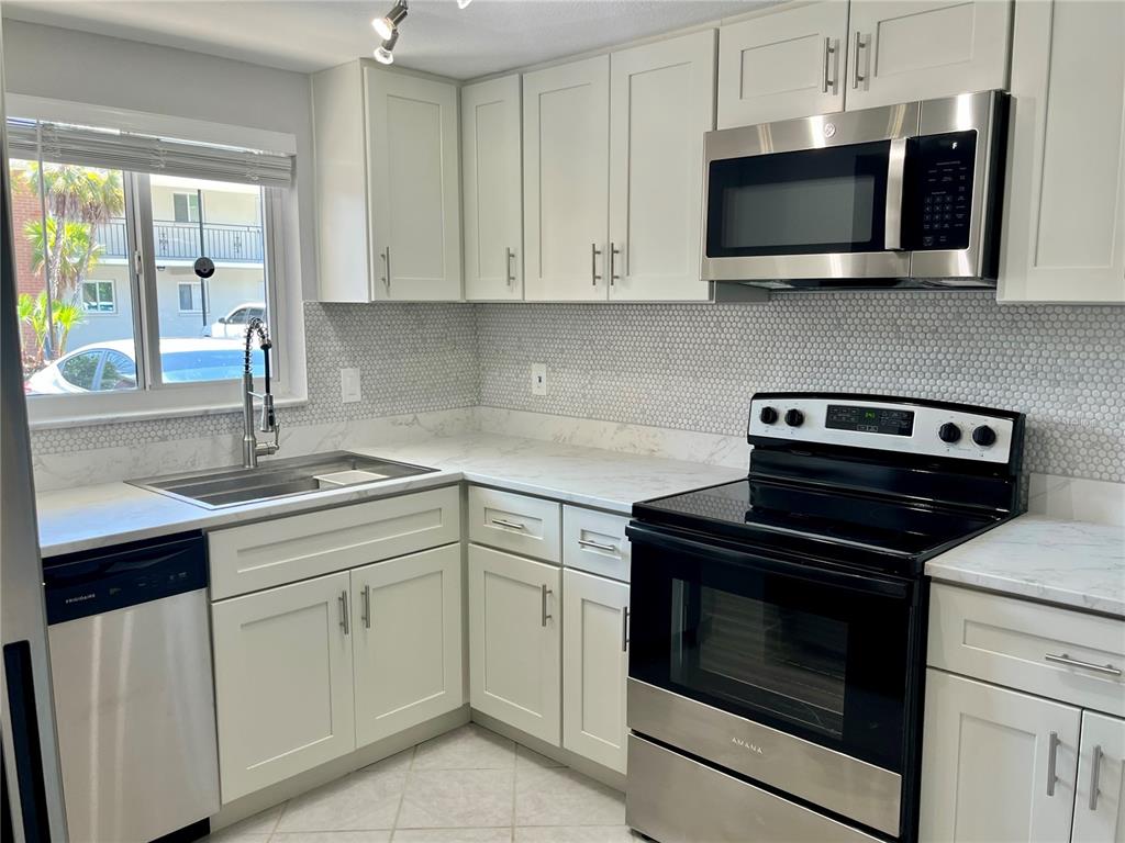 A kitchen features white shaker cabinets, stainless steel appliances, a marble-look countertop, and penny tile — 4550 OVERLOOK DRIVE NE UNIT 156, ST PETERSBURG, FL