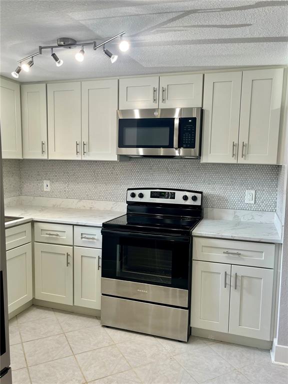 A kitchen features white shaker cabinets, stainless steel appliances, marble-look countertops, and a mosaic backsplash — 4550 OVERLOOK DRIVE NE UNIT 156, ST PETERSBURG, FL