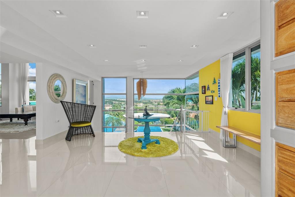 A bright room with white tile floors, a yellow accent wall, and floor-to-ceiling windows — _ ROBLE VALLEY UNIT 12 / 13, HUMACAO, PR
