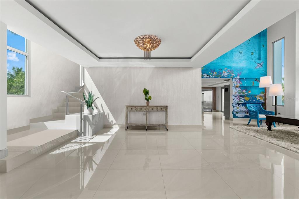 A bright, modern foyer features white tile floors, a central console table, and a staircase — _ ROBLE VALLEY UNIT 12 / 13, HUMACAO, PR