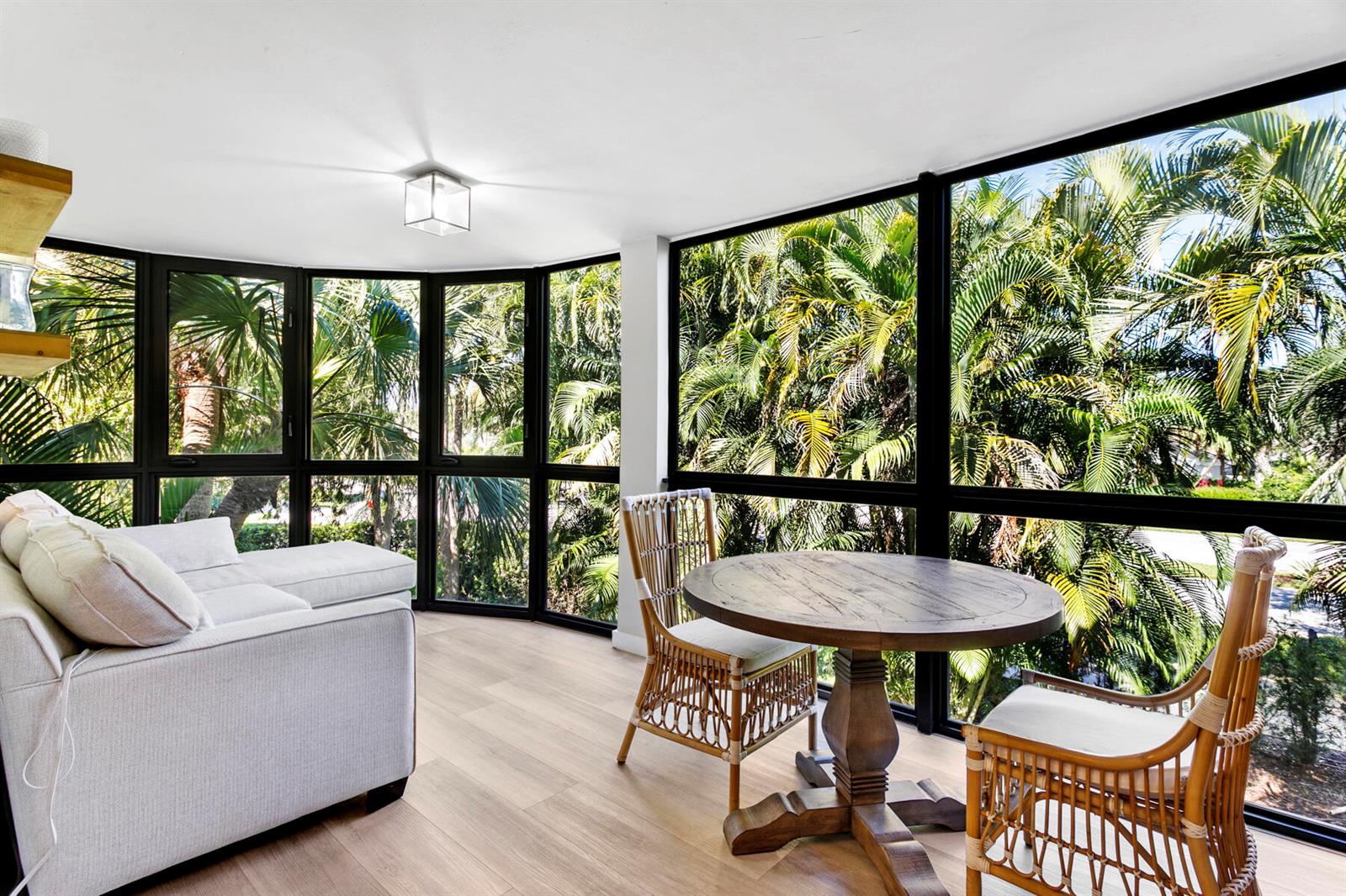 A sunroom with a sofa, a round wooden table, rattan chairs, and large floor-to-ceiling windows — 17137 Waterbend Drive # 201, Jupiter FL 33477, JUPITER, FL
