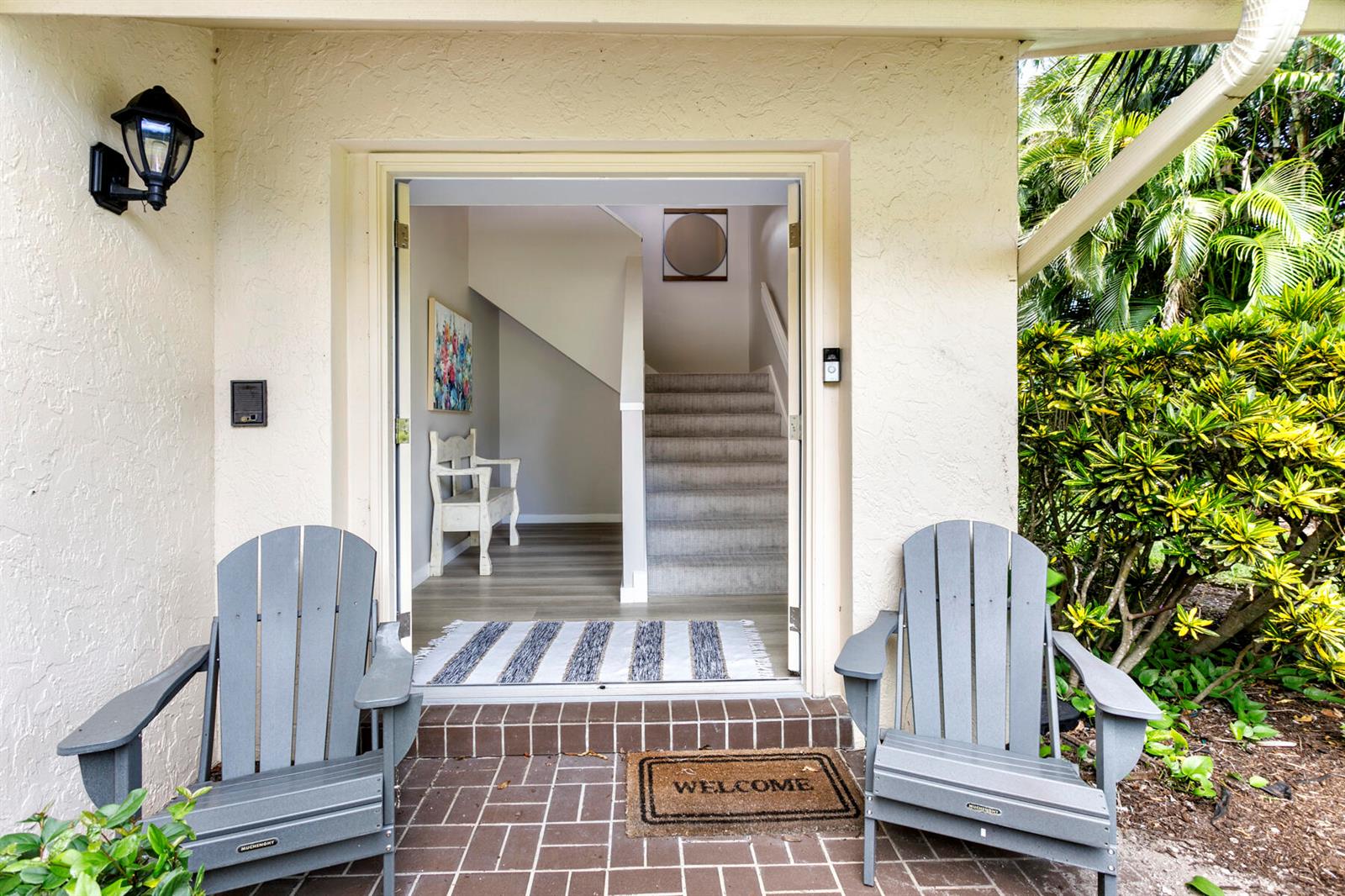 An entryway with two gray Adirondack chairs on a brick patio facing an open doorway — 17137 Waterbend Drive # 201, Jupiter FL 33477, JUPITER, FL
