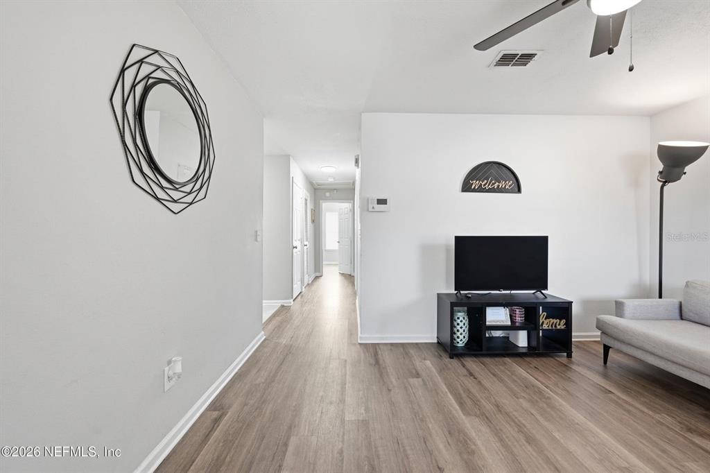 A living room features light wood-look flooring, a television on a black stand, and a mirror — 1233 VAN BUREN STREET, JACKSONVILLE, FL