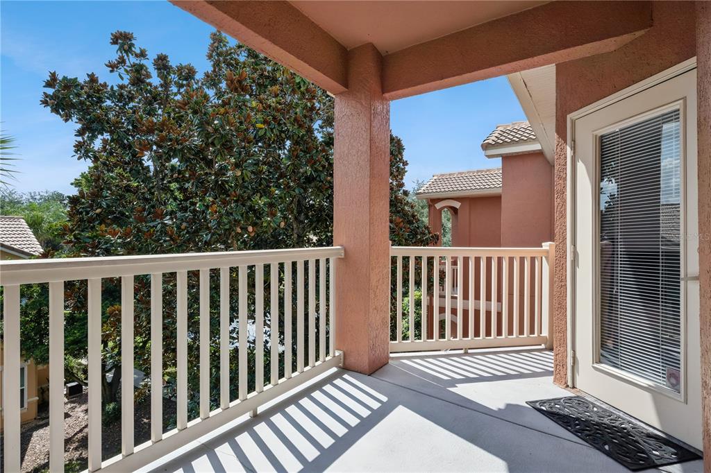 A covered balcony with a white railing overlooks trees and neighboring buildings under a blue sky — 8813 VILLA VIEW CIRCLE UNIT 308, ORLANDO, FL