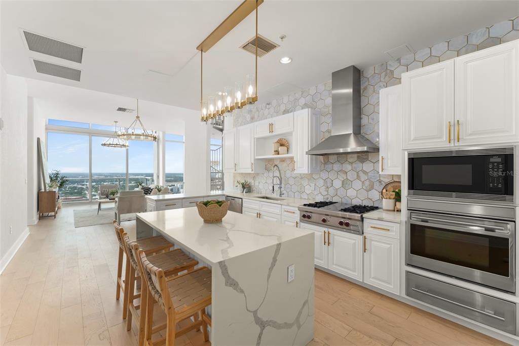 A modern kitchen features white cabinetry, a marble-topped island, and a view of the city — 150 E ROBINSON STREET UNIT PH3504, ORLANDO, FL