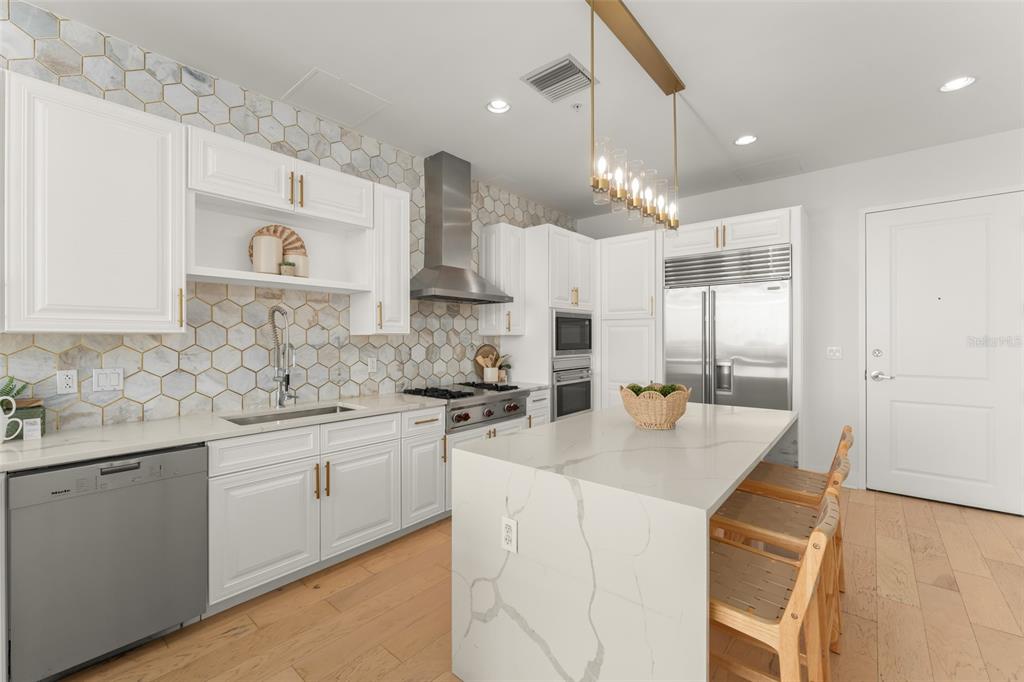 A modern kitchen features white cabinetry, a marble hexagon backsplash, and a large quartz island — 150 E ROBINSON STREET UNIT PH3504, ORLANDO, FL