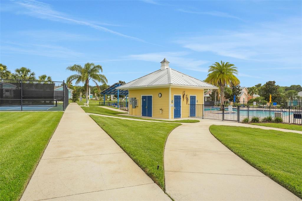 A yellow building with a metal roof sits between a tennis court and a pool — 1026 FIESTA KEY CIRCLE, LADY LAKE, FL