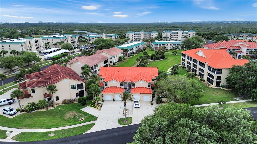 An aerial view shows several multi-story residential buildings with orange tile roofs and landscaping — 441 BOUCHELLE DRIVE UNIT 202, NEW SMYRNA BEACH, FL