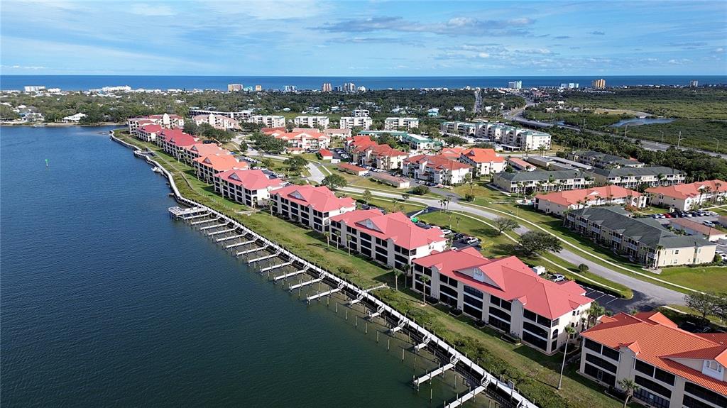An aerial view shows waterfront condominium buildings with red roofs and private boat docks — 441 BOUCHELLE DRIVE UNIT 202, NEW SMYRNA BEACH, FL