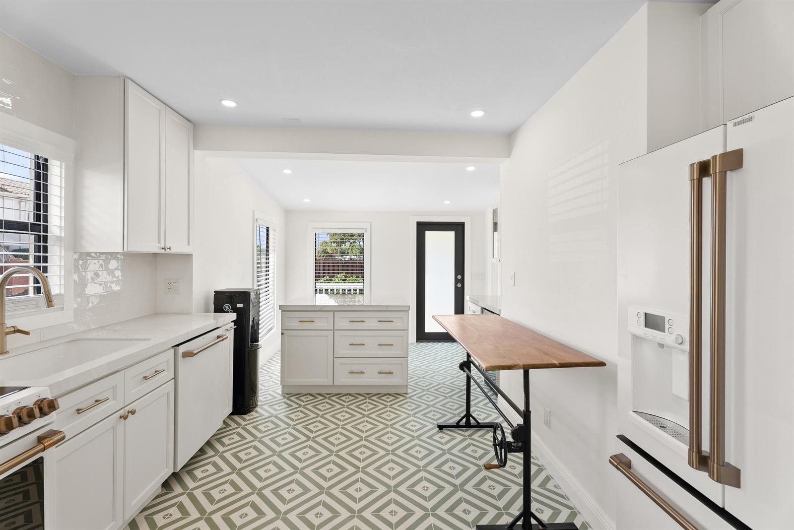 A kitchen features white cabinetry, gold hardware, a wooden table, and patterned floor tiles — 517 55th Street, West Palm Beach FL 33407, WEST PALM BEACH, FL