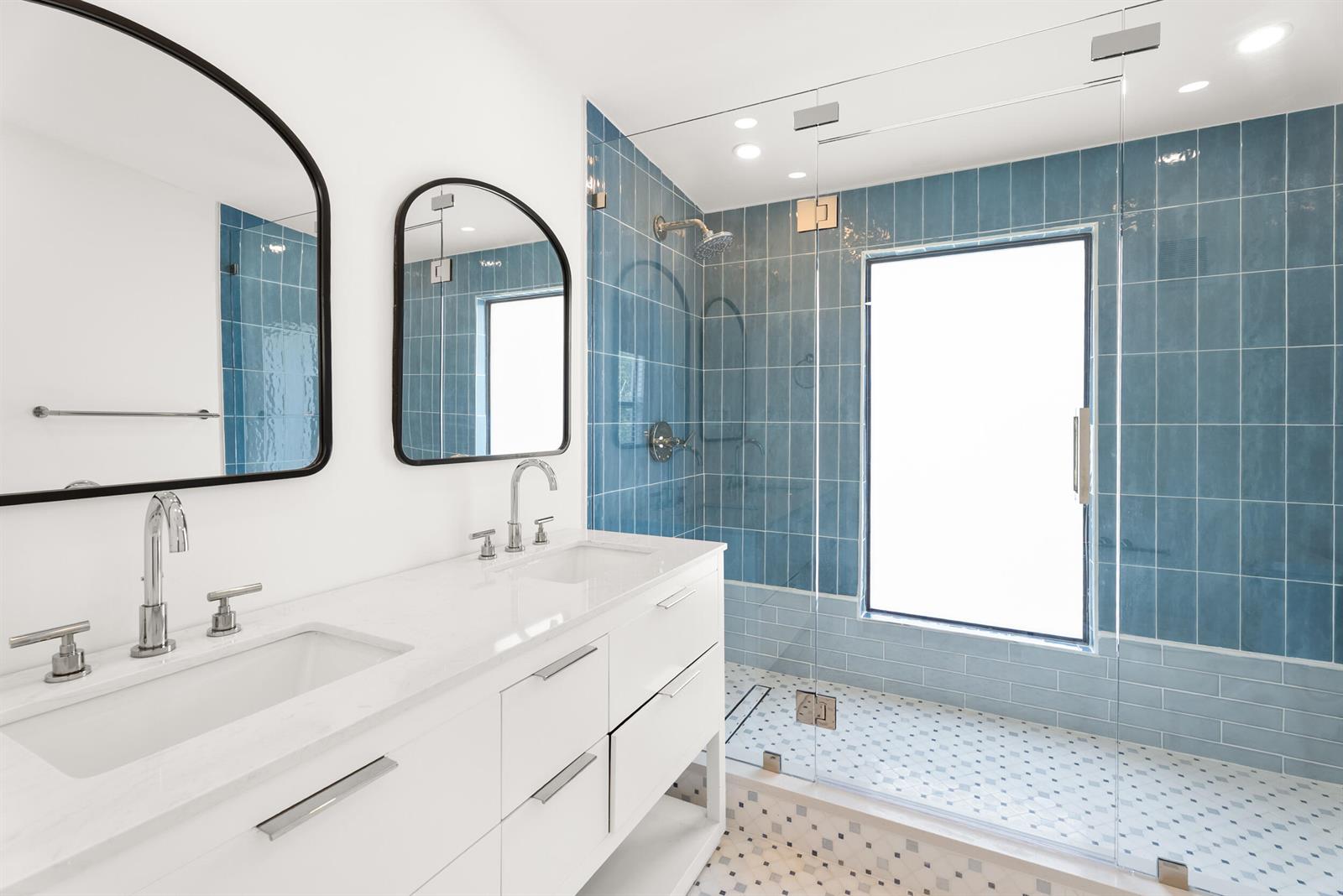 A modern bathroom features a double vanity, arched mirrors, and a blue-tiled walk-in shower — 517 55th Street, West Palm Beach FL 33407, WEST PALM BEACH, FL