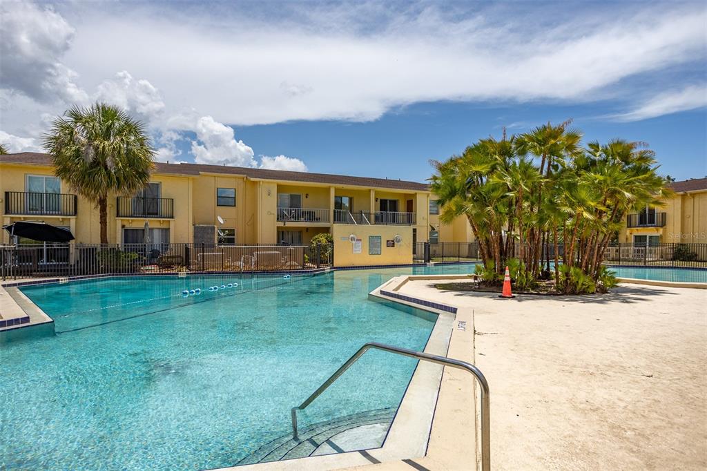 A swimming pool sits in front of a two-story apartment building with palm trees — 7612 NACIDO COURT, TAMPA, FL