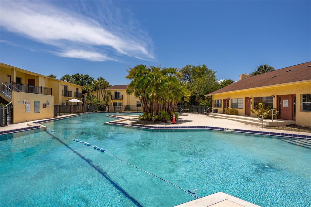 A swimming pool sits in a courtyard surrounded by yellow apartment buildings and palm trees — 7612 NACIDO COURT, TAMPA, FL